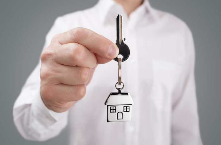 Man holding out house key on a house shaped keychain